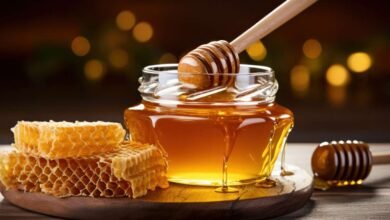 honey dripping from dipper into jar set against wooden tones 11533552591
