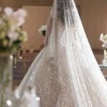 "عروس عربية شابة تتألق بإطلالة أنيقة في العيد، تجلس في مجلس منزل عصري مزين بديكورات العيد، تستقبل الضيوف بابتسامة وتقدم القهوة والحلويات التقليدية في أجواء عائلية دافئة."